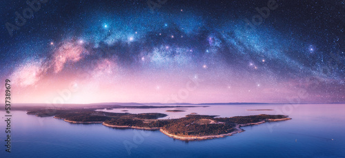 Milky Way arch and islands in the sea at summer night. Kamenjak cape, Adriatic sea, Croatia. Landscape with purple starry sky, arched milky way, sea coast, water, mountains. Top view. Panorama © den-belitsky