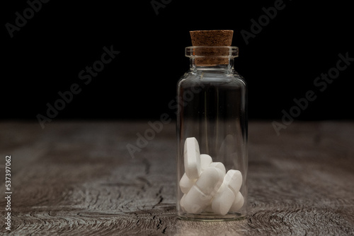 Glass bottle with white pills on a wooden table. the Container is located on a dark background.