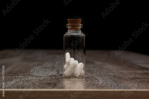 Glass bottle with white pills on a wooden table. the Container is located on a dark background.