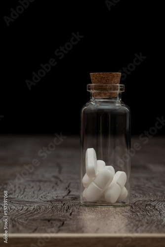 Glass bottle with white pills on a wooden table. the Container is located on a dark background.
