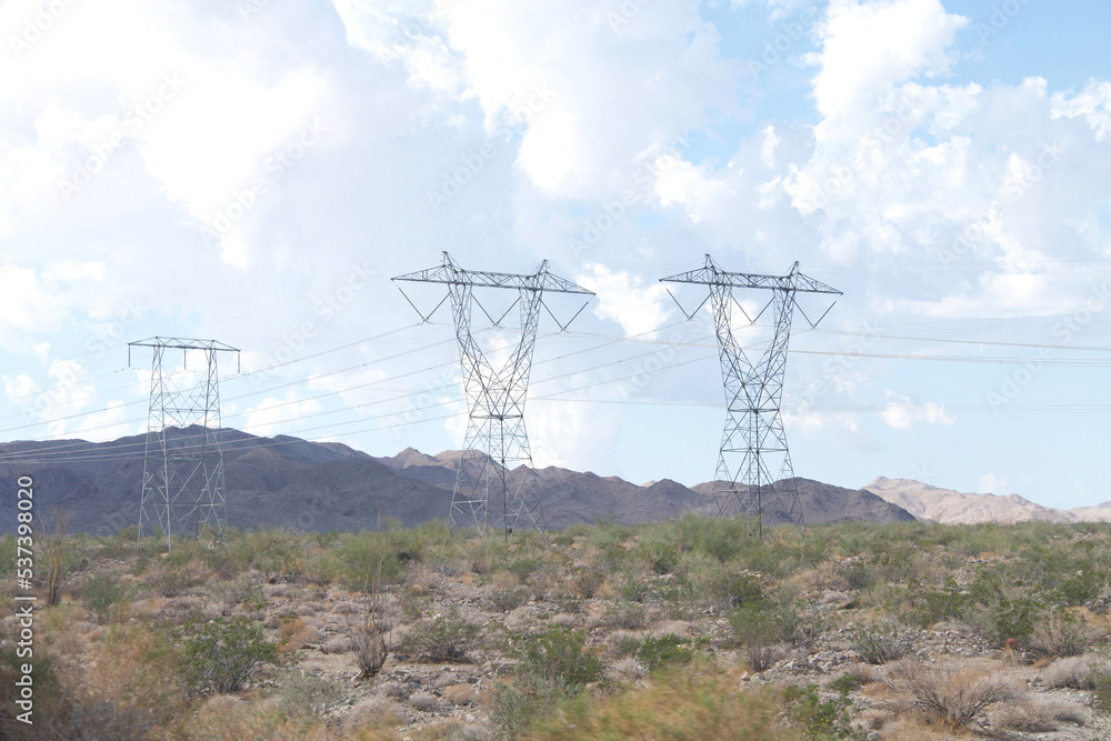 Large tall power lines running through desert landscape with mountains in the background. Blue skies with white clouds. Large tall power lines running through desert landscape with mountains in the background. Blue skies with white clouds.