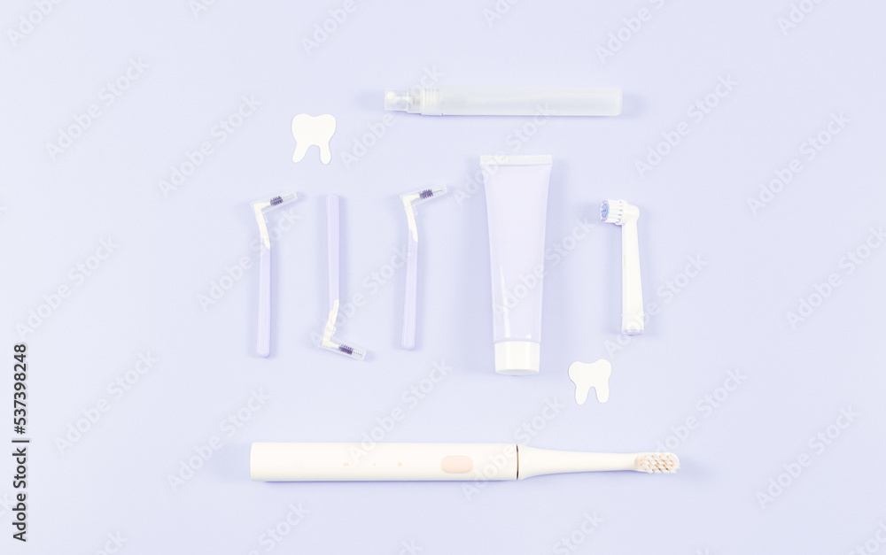Obraz premium A set of small toothbrushes, toothpaste, an electric toothbrush and paper teeth on soft lilac.