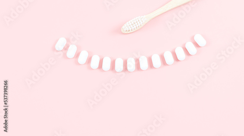 A bamboo toothbrush and chewing gums in a smile on a soft pink