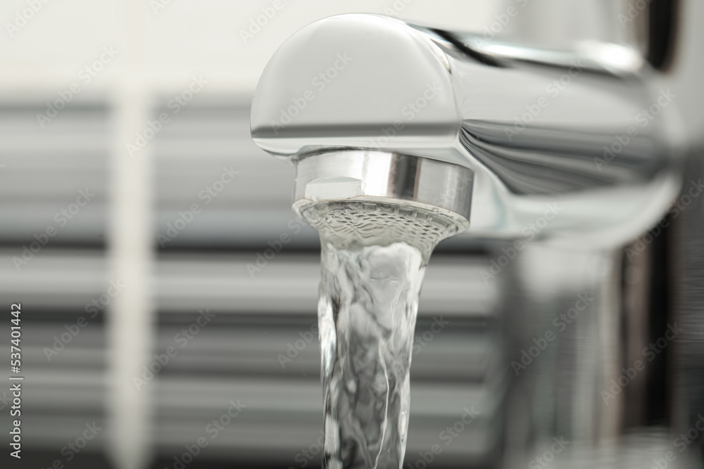 Water flowing from tap on blurred background, closeup. Space for text Water flowing from tap on blurred background, closeup. Space for text