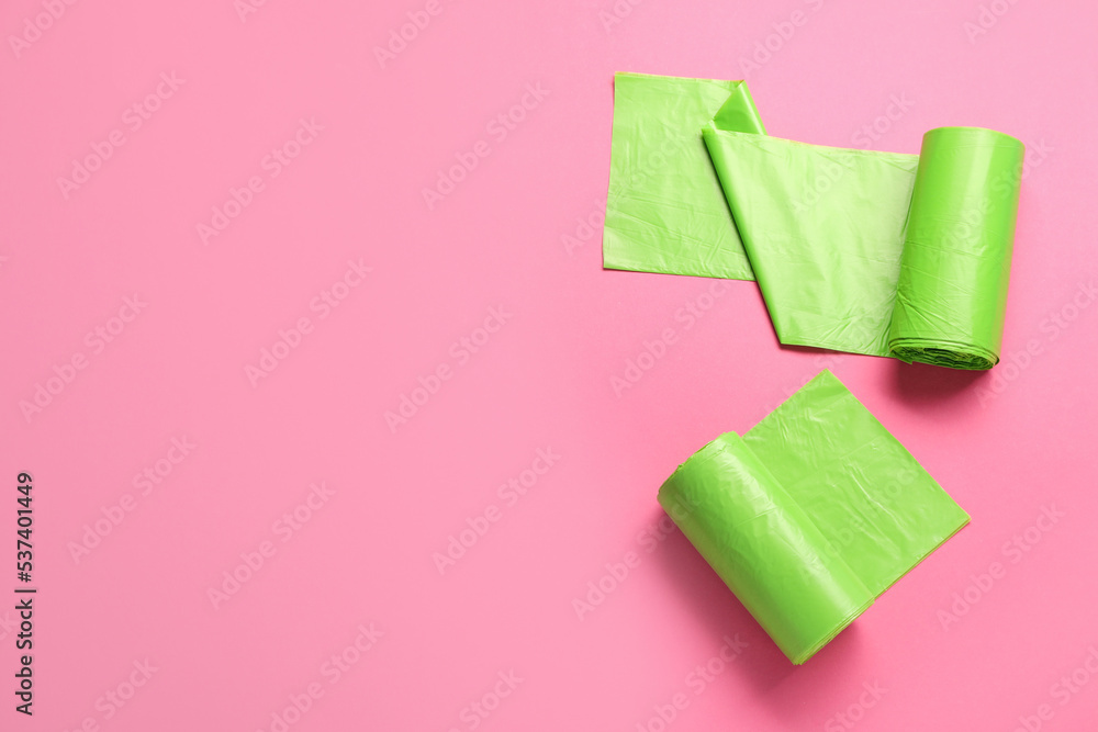 Fototapeta premium Rolls of green garbage bags on pink background, flat lay. Space for text