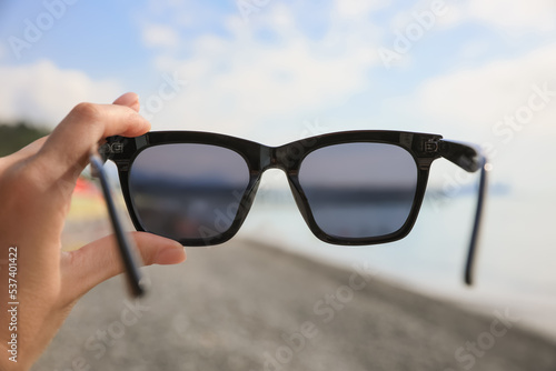 Woman holding sunglasses near sea on sunny day, closeup