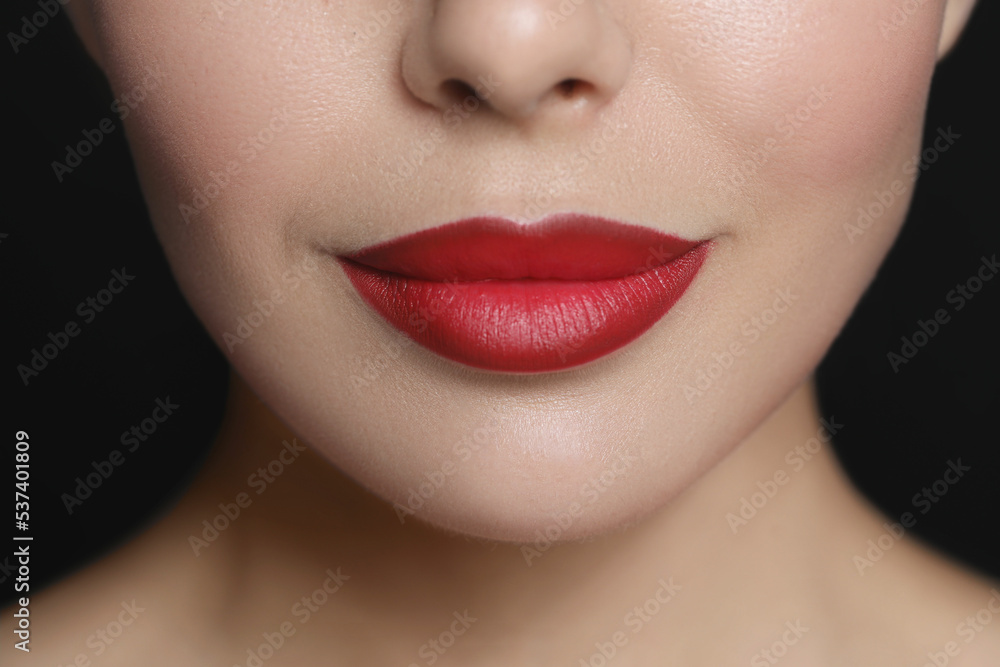 Young woman wearing beautiful red lipstick on black background, closeup Young woman wearing beautiful red lipstick on black background, closeup