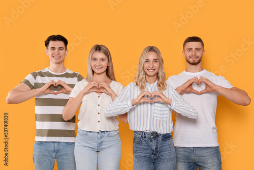 Happy volunteers making hearts with their hands on orange background