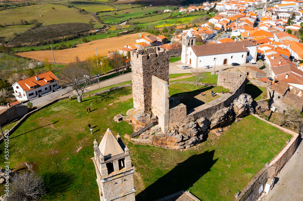 Aerial view of remains of medieval fortified stone castle in Portuguese township of Mogadouro towering above terracotta roofed residential buildings on sunny spring day