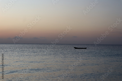 Kendwa, Zanzibar Island, Tanzania solo fishing boat against the setting sun and cloudy sky.