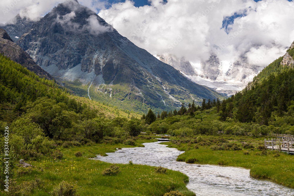 Yangmaiyong Snow Mountain, Yading Scenic Spot, Ganzi Daocheng, Sichuan, stream of the river, clouds in the sky Yangmaiyong Snow Mountain, Yading Scenic Spot, Ganzi Daocheng, Sichuan, stream of the river, clouds in the sky