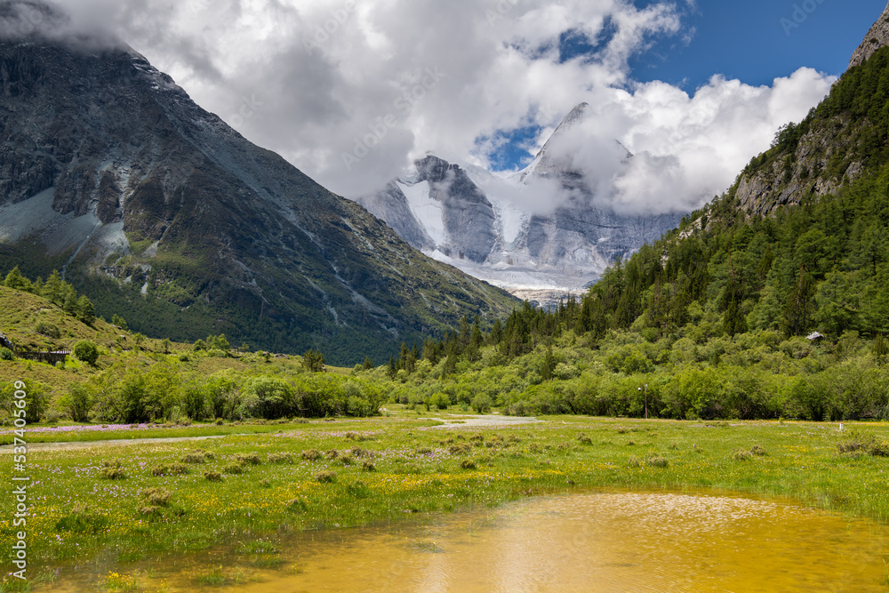 View of the sacred Mount Jampayang (Chinese: Yangmaiyong) covered with clouds with Chonggu meadow and river at Yading Nature Reserve in Daocheng county, southwest of Sichuan Province, China.