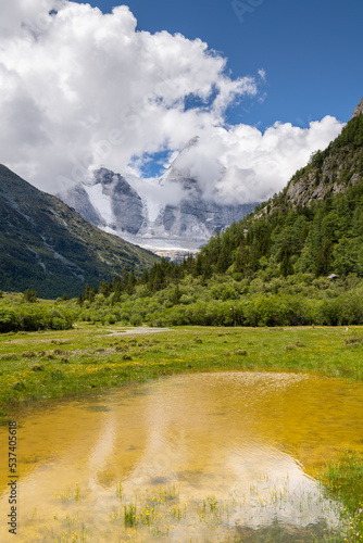 View of snow covered mountain peaks, yellow river waters and lue sky covered with clouds in Yading Nature reserve, Sichuan, China. Beautiful nature landscape.