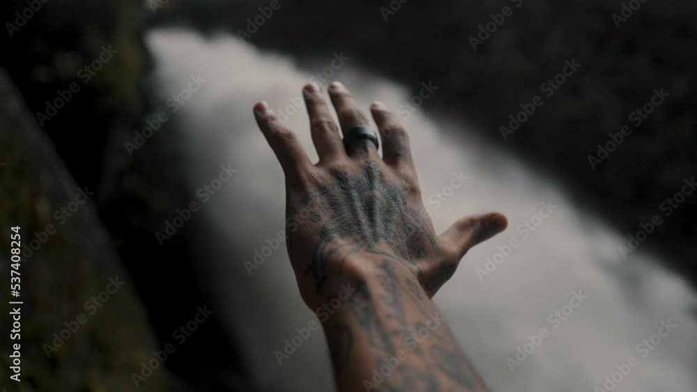 Male Hand With Tattoo Reaches Toward A Waterfall (Pailon del Diablo Waterfall, Baños de Agua Santa, Ecuador) - selective focus Male Hand With Tattoo Reaches Toward A Waterfall (Pailon del Diablo Waterfall, Baños de Agua Santa, Ecuador) - selective focus