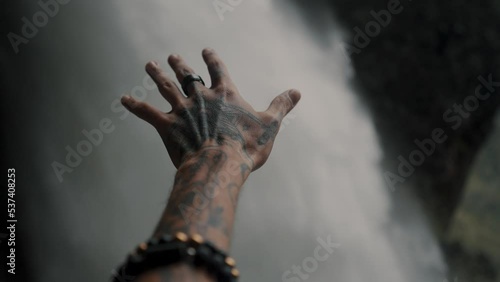 Tattooed Hand Reaching Pailon Del Diablo Waterfall In Baños De Agua Santa, Ecuador. Selective Focus