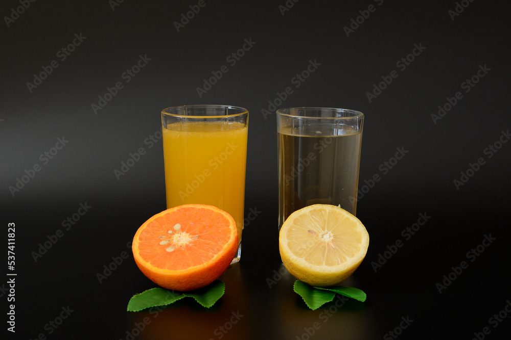 Two glasses with lemon and orange juice decorated with leaves and citrus halves on a black background. Two glasses with lemon and orange juice decorated with leaves and citrus halves on a black background.