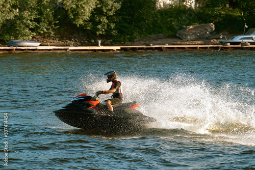A young man floats on a jet ski along the river along the shore at high speed. The guy is engaged in extreme sport.