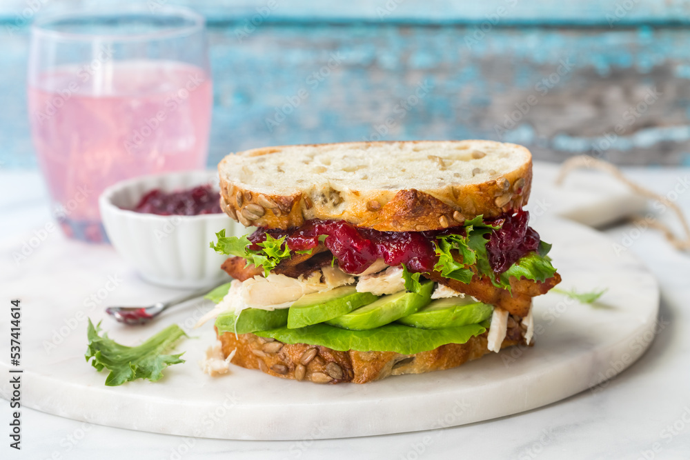 A turkey sandwich with avocado and cranberry sauce on multigrain bread.