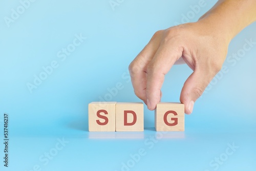 SDG or Sustainable development goals concept. Human hand stacking wooden blocks in blue background
