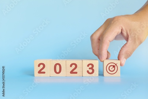 Start New Year 2023 business target goal concept. Human hand stacking wooden blocks with 2023 target icon.