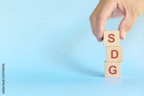 SDG or Sustainable development goals concept. Human hand stacking wooden blocks in blue background