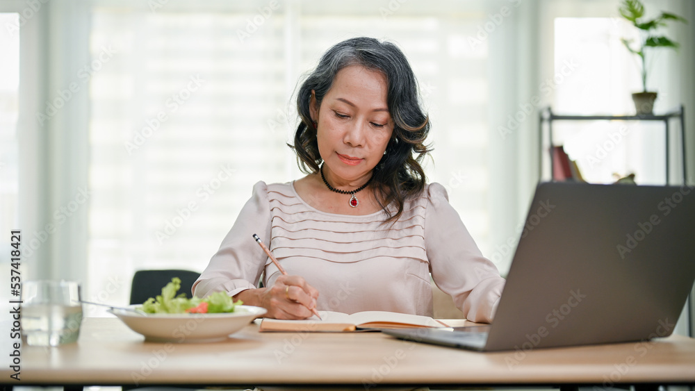 Beautiful senior asian businesswoman working from home, focused on writing at her desk. Beautiful senior asian businesswoman working from home, focused on writing at her desk.