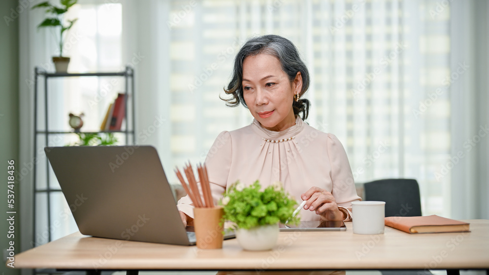 Professional 60s aged-asian businesswoman or teacher working, looking at laptop screen. Professional 60s aged-asian businesswoman or teacher working, looking at laptop screen.