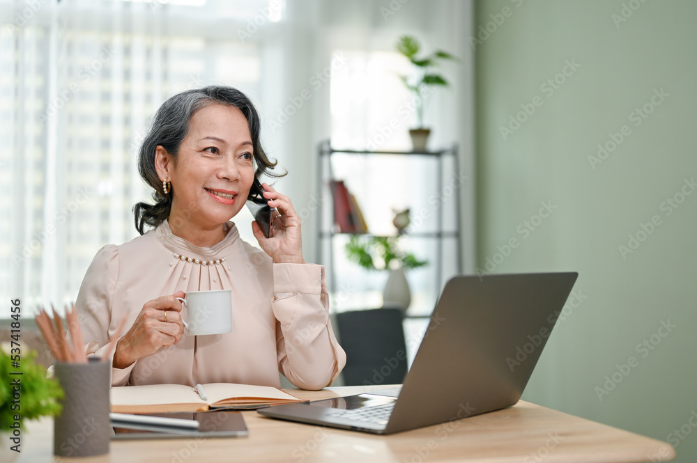 Attractive aged Asian businesswoman talking on the phone with her business partner Attractive aged Asian businesswoman talking on the phone with her business partner
