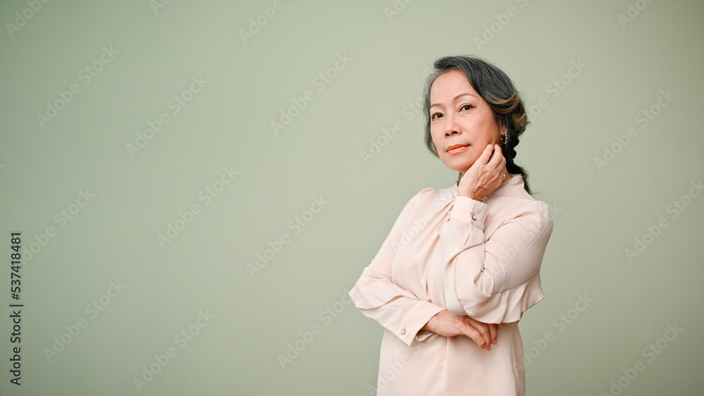 Gorgeous 60s aged-asian woman arm crossed, hand on chin, looking at camera, isplated background Gorgeous 60s aged-asian woman arm crossed, hand on chin, looking at camera, isplated background