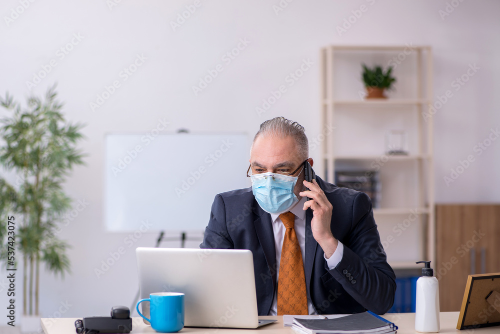 Old male employee working in the office during pandemic
