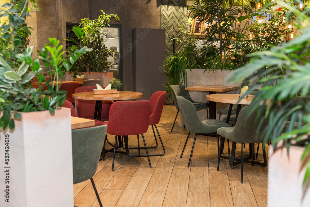 Naklejka premium Cozy cafe interior without visitors. Modern design with large plants and wooden tables.
