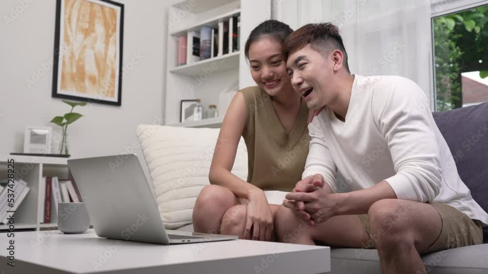 Asian couple using laptop to connect with family for video call. Man and Woman using laptop computer in living room at home. Asian couple using laptop to connect with family for video call. Man and Woman using laptop computer in living room at home.