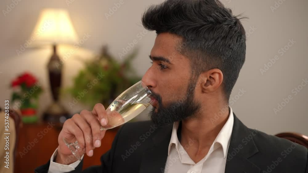 Close-up of confident Middle Eastern young handsome man talking clinking glass drinking champagne. Portrait of happy relaxed guy celebrating Christmas with friends sitting at dinner table indoors Close-up of confident Middle Eastern young handsome man talking clinking glass drinking champagne. Portrait of happy relaxed guy celebrating Christmas with friends sitting at dinner table indoors