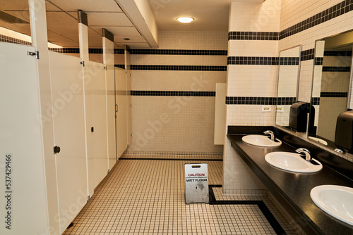 Modern Bathroom Interior with Bathroom Sinks, Bathroom Stalls and Caution Wet Floor Sign  