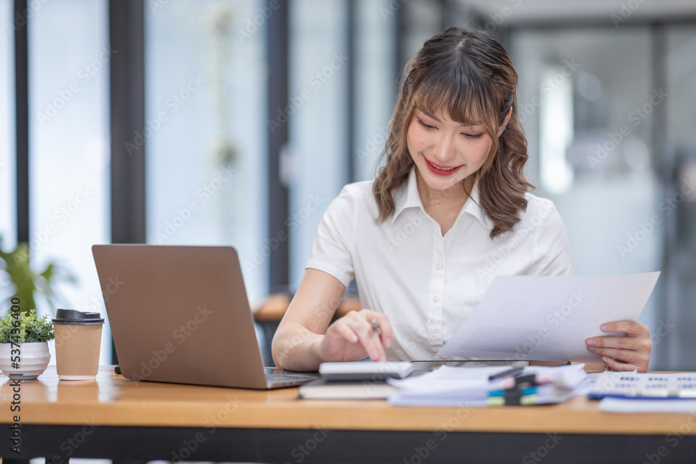 Young Business Asian woman using calculator and laptop for doing math finance on an workplace, tax, report, accounting, statistics, and analytical research concept. Young Business Asian woman using calculator and laptop for doing math finance on an workplace, tax, report, accounting, statistics, and analytical research concept.