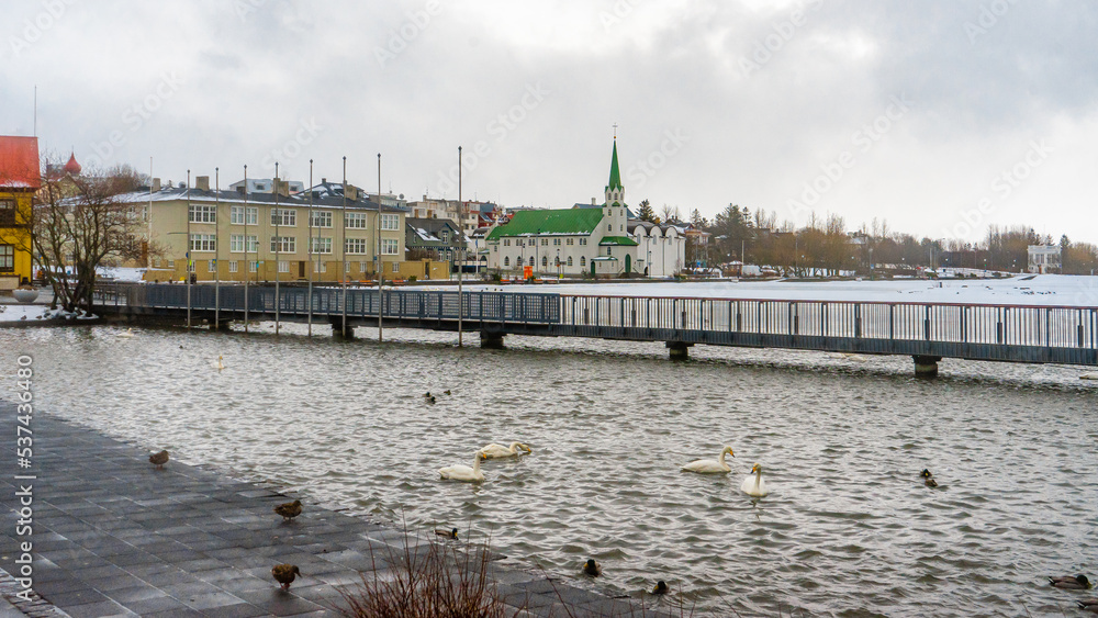 Fototapeta premium Tjornin Viewpoint lake and buildings next to the Reykjavik City Hall during winter cloudy day in Reykjavik , The Capital of Iceland : 21 March 2020
