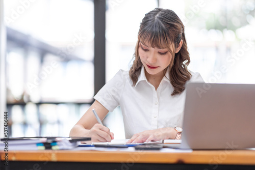 Young Business Asian woman using calculator and laptop for doing math finance on an workplace, tax, report, accounting, statistics, and analytical research concept.