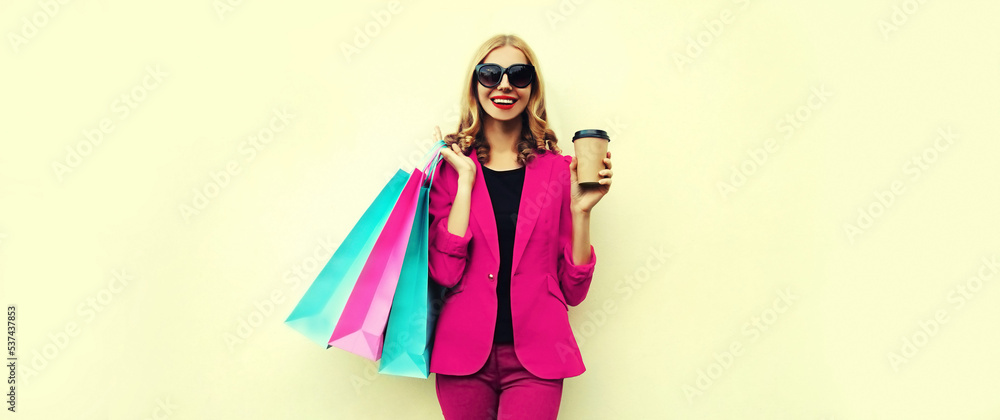 Portrait of beautiful happy smiling young woman with colorful shopping bags and cup of coffee wearing pink business blazer on background Portrait of beautiful happy smiling young woman with colorful shopping bags and cup of coffee wearing pink business blazer on background