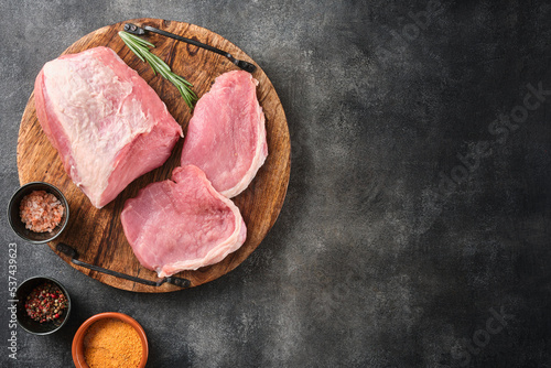 Raw pork meat on wooden board on grey background  with rosemary, salt and pepper. Pork loin. Copy space. Top view.