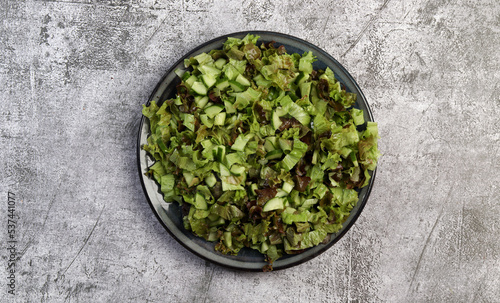 Lettuce and cucumber salad on a round plate on a dark gray background. Top view  flat lay.