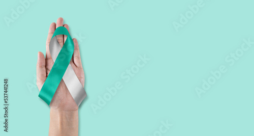 Teal and white ribbon for cervical cancer awareness month in January and HPV prevention with bow on hand support photo