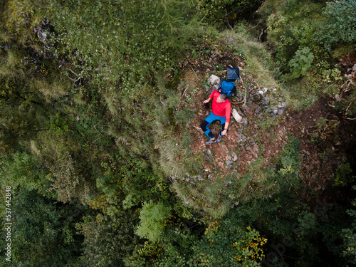 Hiker, middle-aged climber is on rock, surrounded by forest and makes recording of himself with a drone, lilienfeld, austria