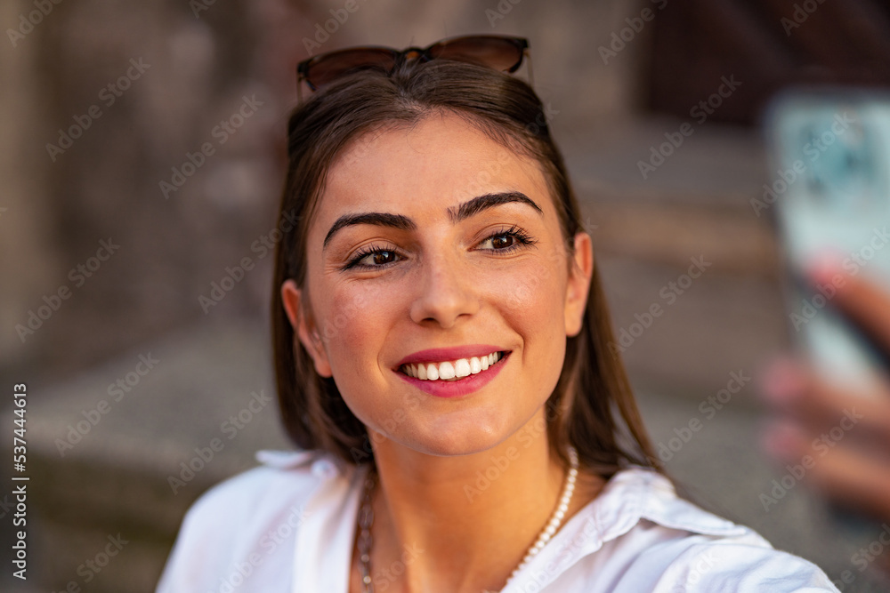Portrait of a pretty happy young girl sitting on a stairs in old european town, taking a selfie with mobile phone Portrait of a pretty happy young girl sitting on a stairs in old european town, taking a selfie with mobile phone