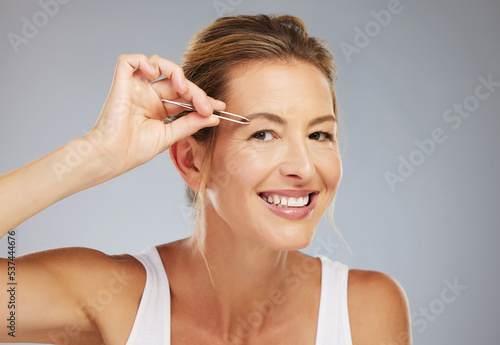 Face, eyebrows and senior woman plucking hair for beauty, wellness and clean body against a grey mockup studio background. Portrait of an elderly model doing skincare with tweezers and mock up space