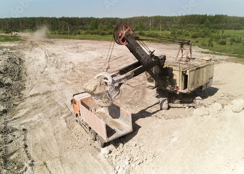 Shovel excavator loads truck with chalk at quarry in summer