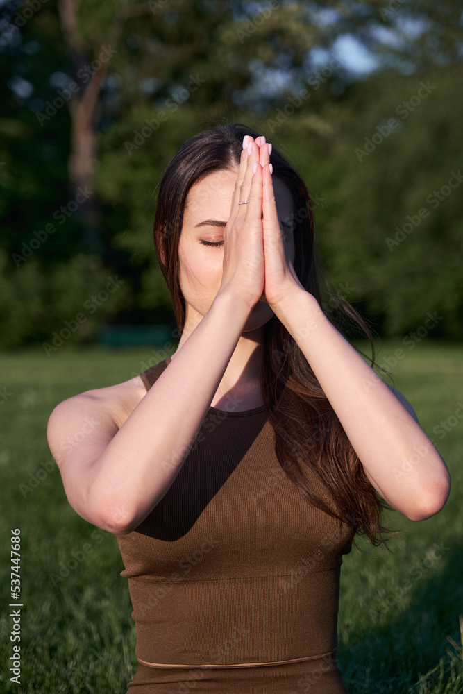 A young woman practices yoga while lying on a mat in the park.