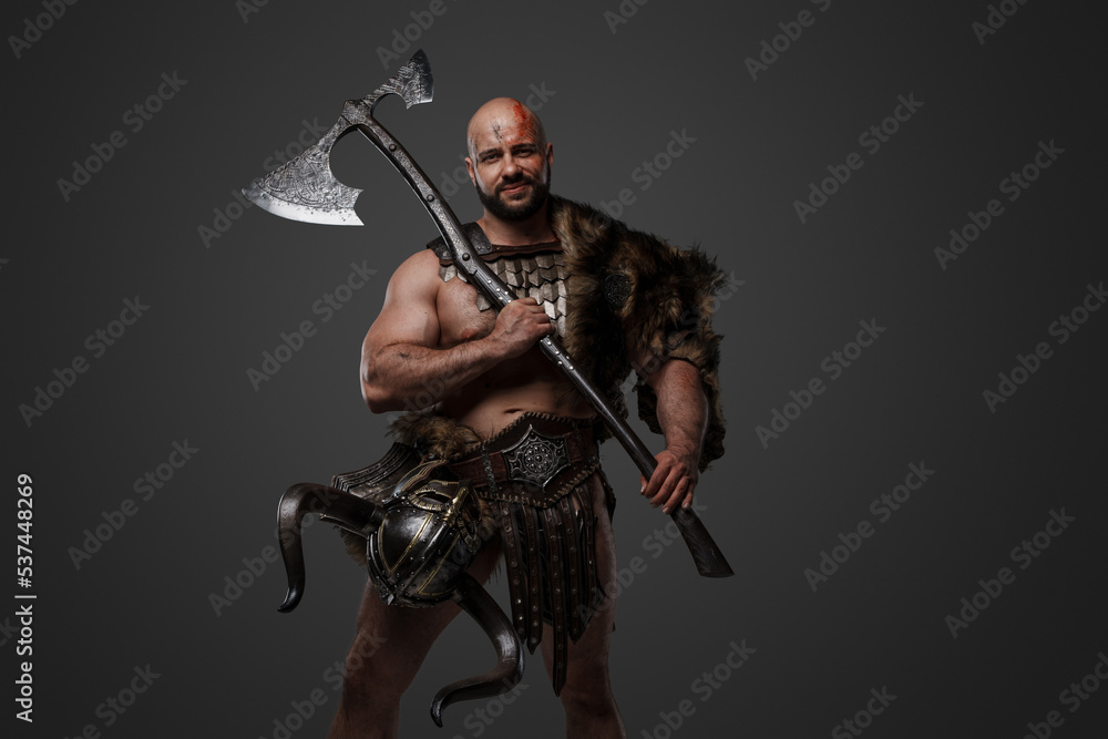 Naklejka premium Shot of scandinavian barbarian with fur and horned helmet holding two handed axe.
