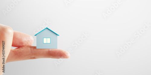 Mortgage concept with small blue house layout on human finger on blank light background with place for advertising poster or your logo  mock up