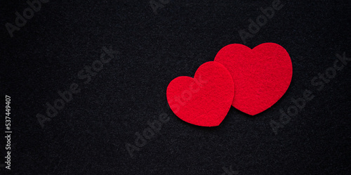 Two red hearts made of fabric on a black background.Romantic background for the ad. A red heart carved out of felt.