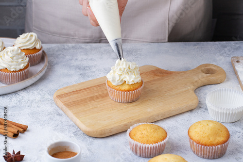 A pastry bag applies cream to a cupcake